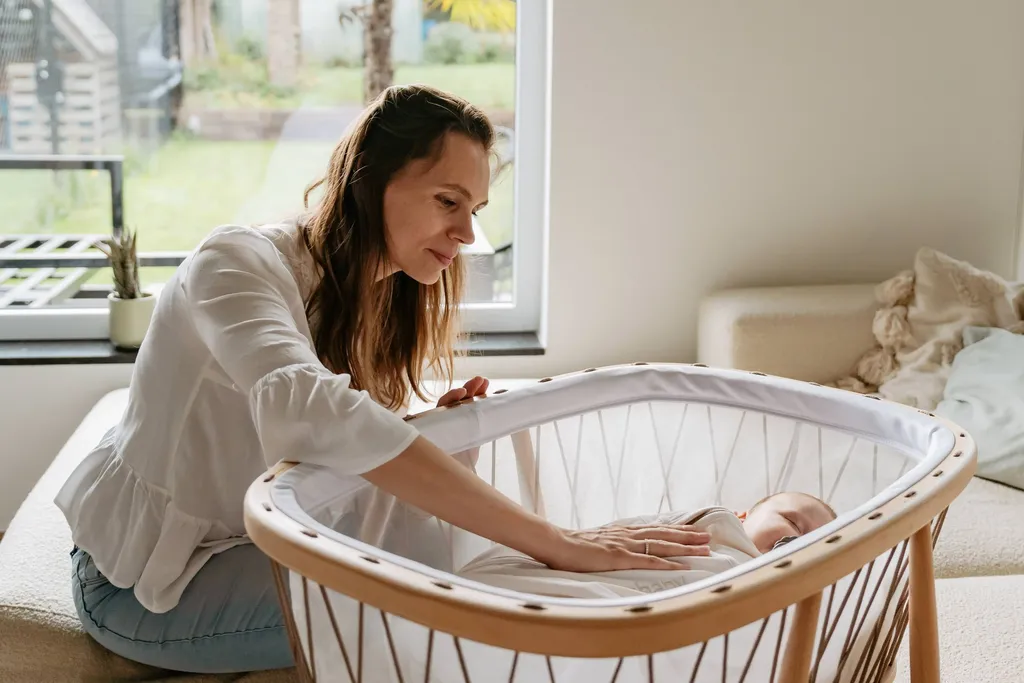 Een vrouw raakt zachtjes een slapende baby aan in een modern wiegje.