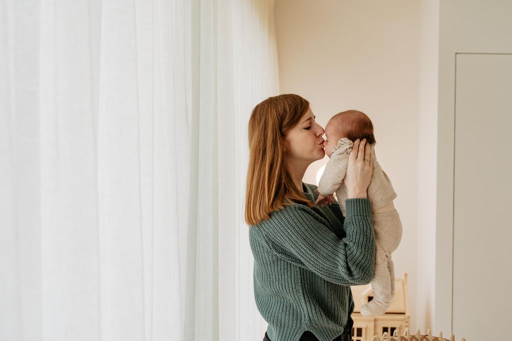 A woman with long hair gently kisses a baby on the forehead.