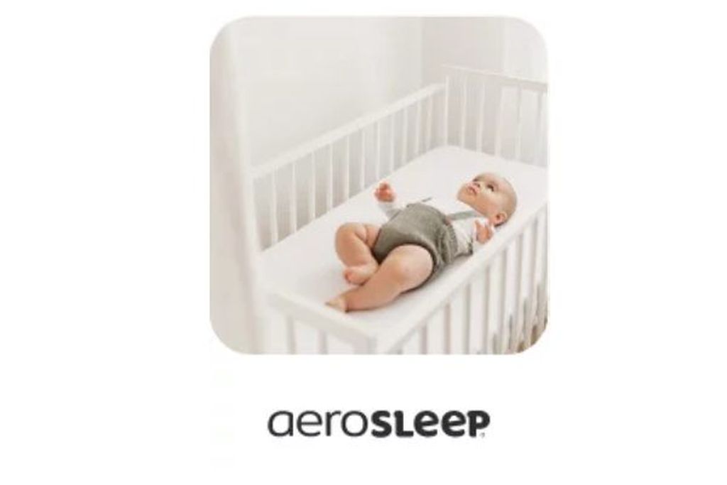 Ein Baby liegt auf einer weißen Matratze in einem Kinderbett mit einer AeroSleep-Matratze und einem perforierten Spannbetttuch