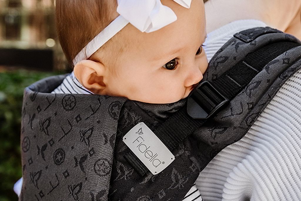 Ein Baby wird in einer Fidella-Babytrage auf dem Rücken getragen.