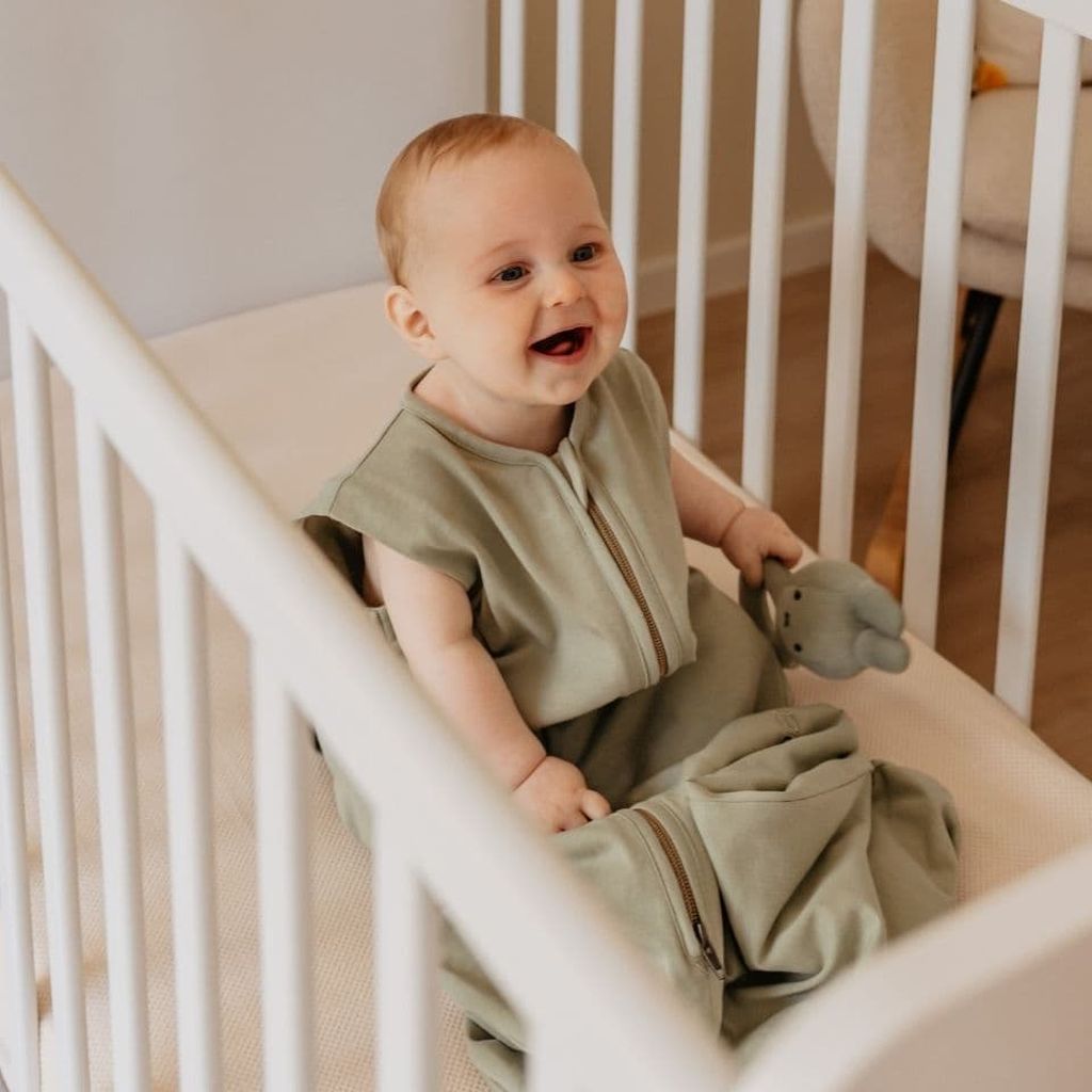 Smiling toddler in sleep back sitting on a bed