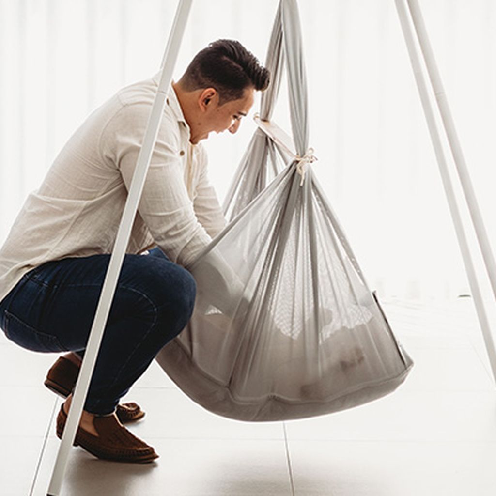 A man crouches beside a gray baby hammock, gently adjusting it