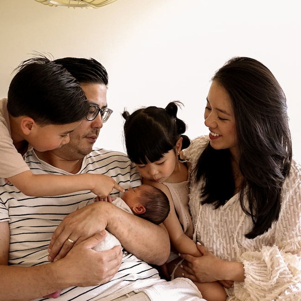 Eine vierköpfige Familie, bewundert liebevoll ein Neugeborenes, das der Vater in seinen Armen wiegt