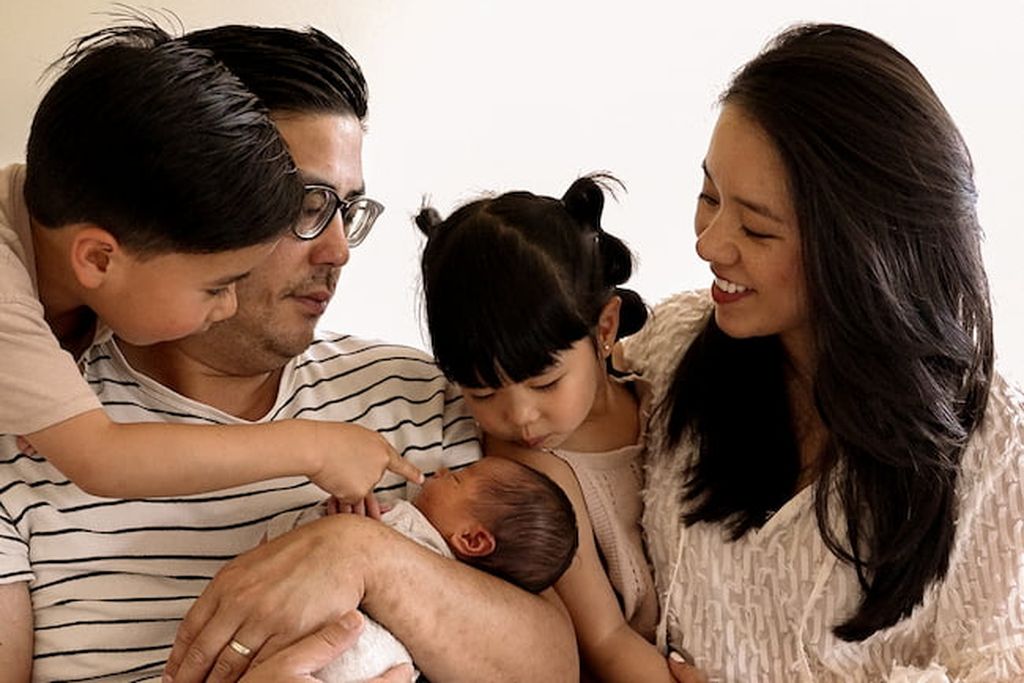 Eine vierköpfige Familie, bewundert liebevoll ein Neugeborenes, das der Vater in seinen Armen wiegt