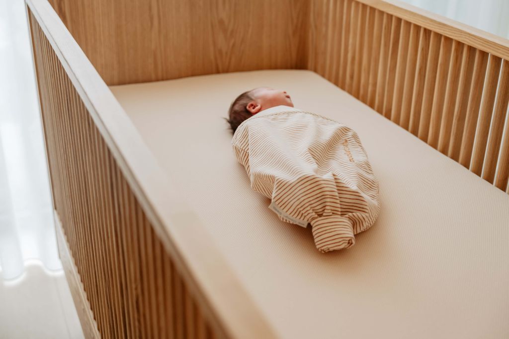 Een baby slaapt vredig op een geperforeerd AeroSleep-hoeslaken.