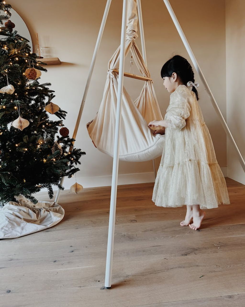 Ein Kind in einem weißen Kleid steht neben einer Federwiege im Tipi Gestell