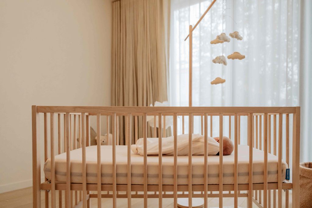 Een slapende baby ligt in een ledikant op een AeroSleep Evolution-matras.