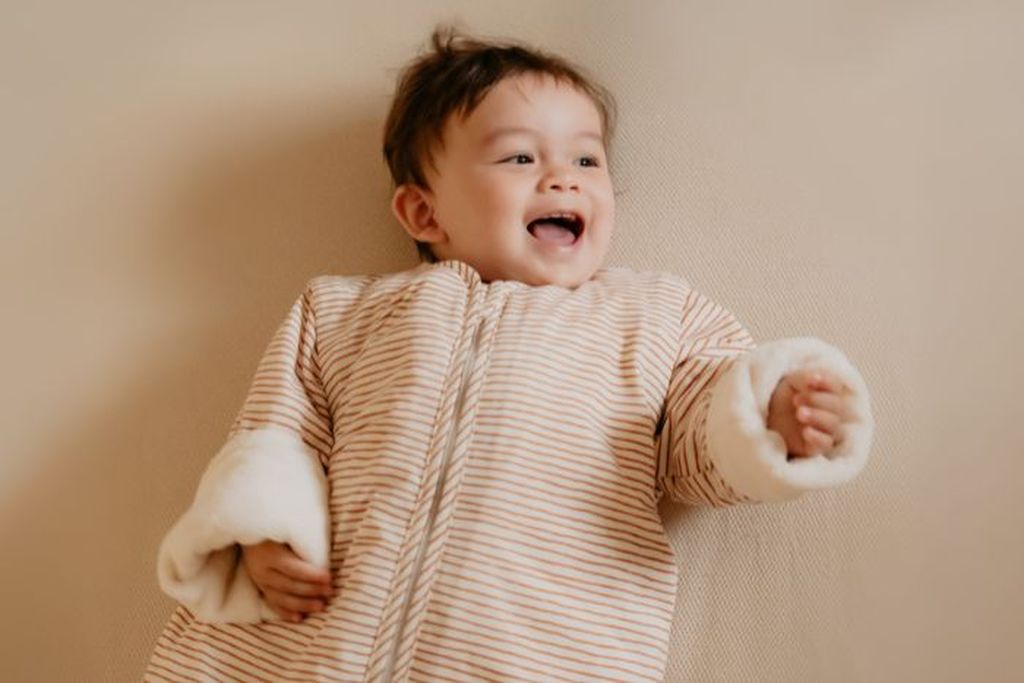 Baby in een Bag 4 Seasons slaapzak die op bed ligt en lacht