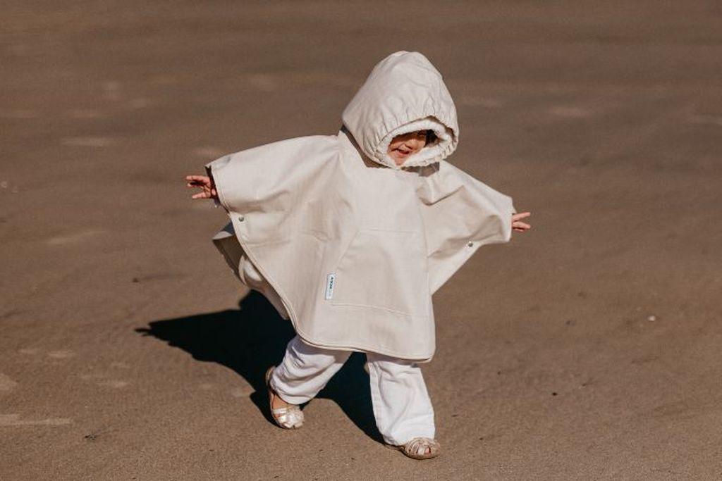 Meisje met regen- en winterponcho van AeroMoov aan het strand