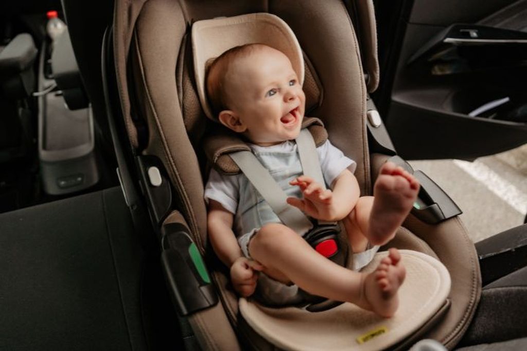 Een vrolijke baby zit in zijn autostoel met een Air Layer geïnstalleerd.