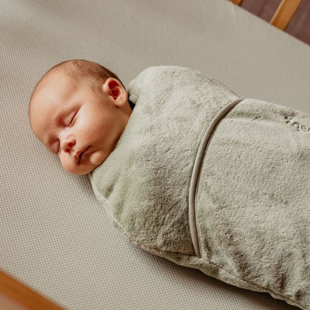 A sleeping baby wrapped snugly in a soft, light green blanket on a cushioned surface.