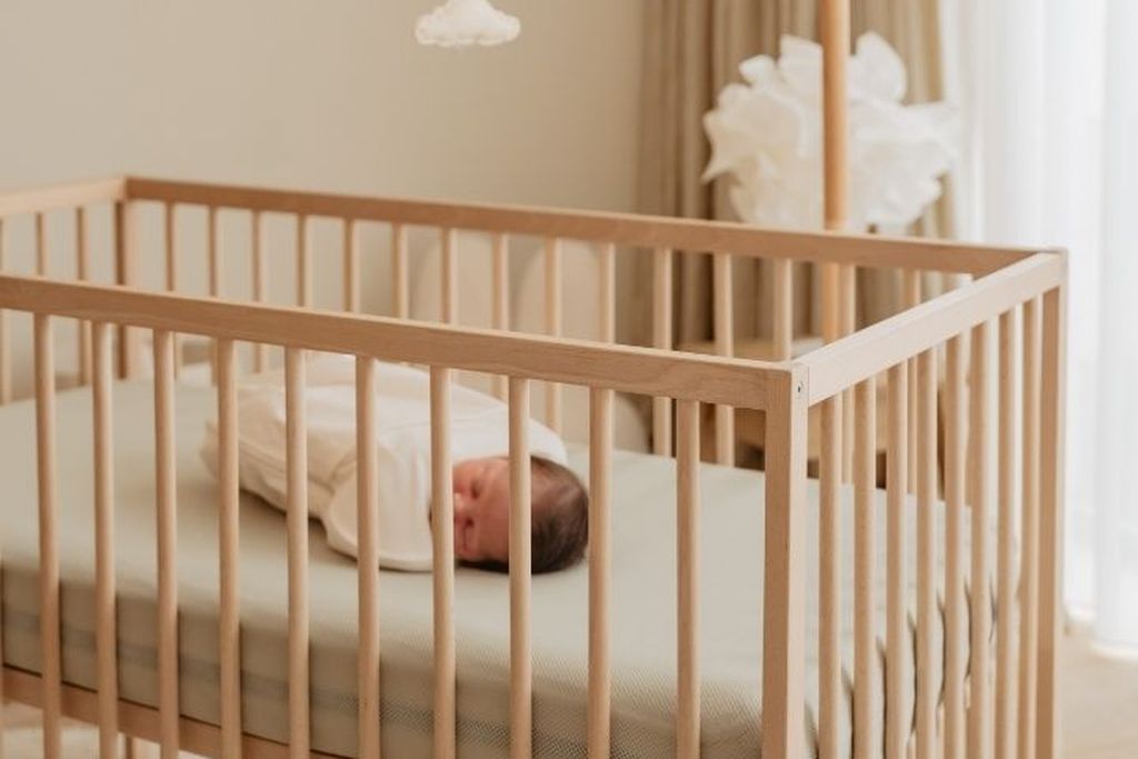 Baby ligt in een wiegje op een Aerosleep matras met hoeslaken in een babykamer