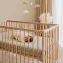 A baby wearing a swaddle bag, sleeps in a wooden crib on a aerosleep mattress a warmly lit room