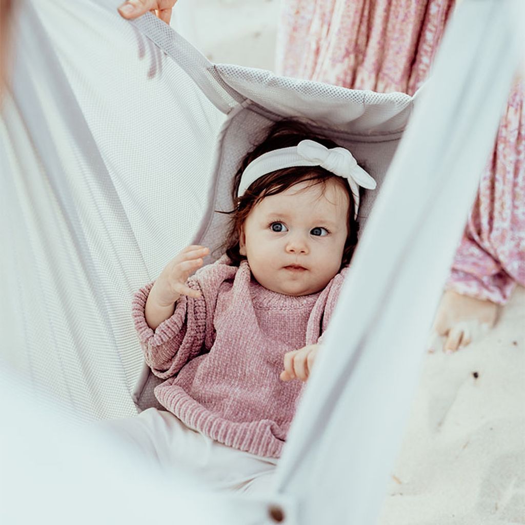 Baby mit rosa Pullover und weißem Stirnband, das in der Federwiege liegt