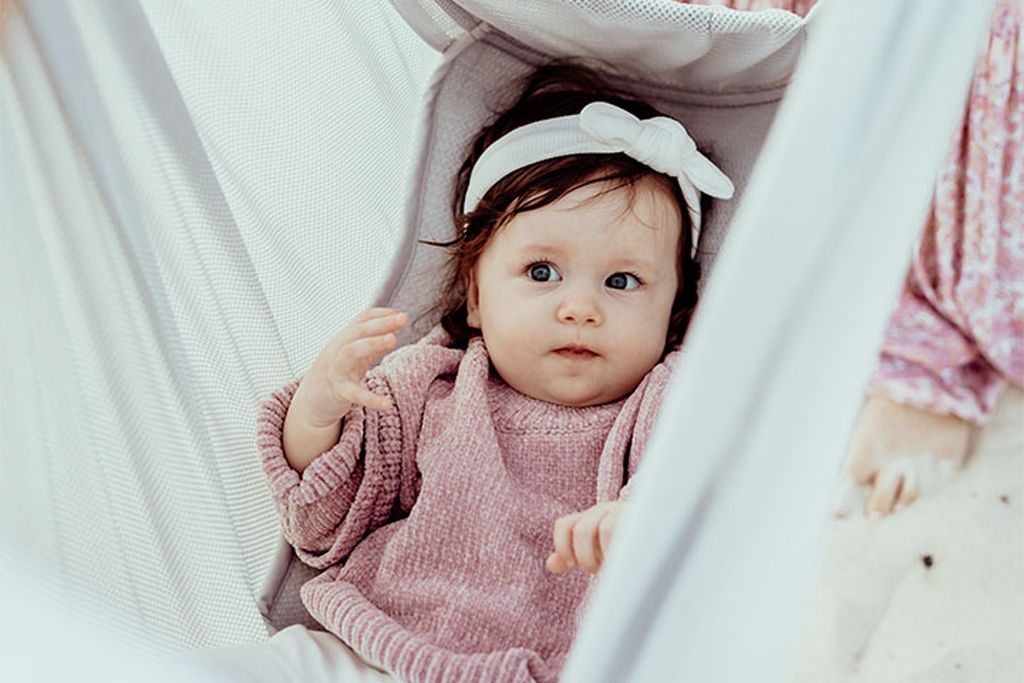 Baby mit rosa Pullover und weißem Stirnband, das in der Federwiege liegt