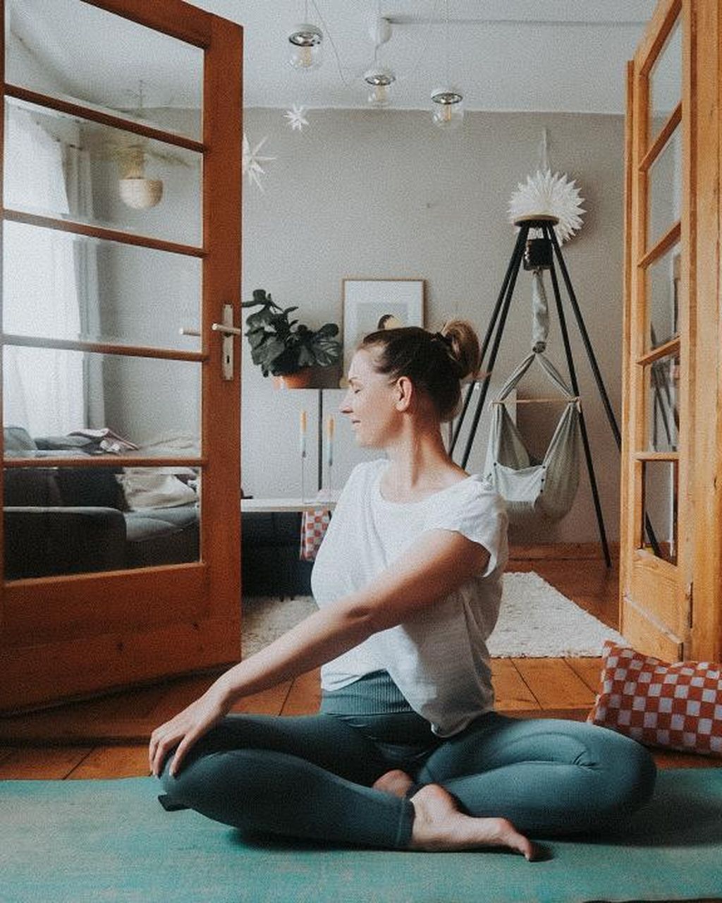 Frau, die in einem gemütlichen Wohnzimmer Yoga macht, mit der NONOMO Federwiege im Hintergrund