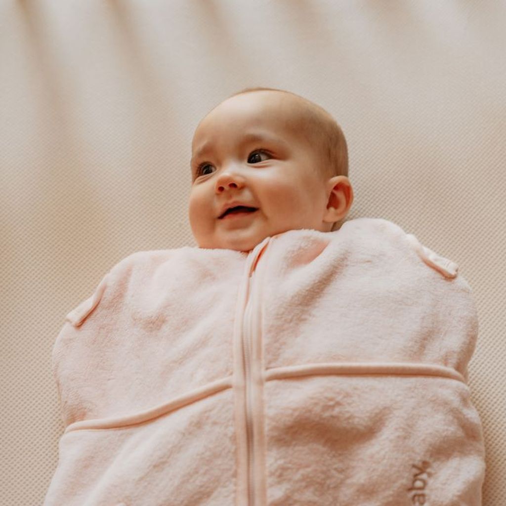 Smiling baby wrapped in a soft, pink swaddle blanket, looking content and cozy.
