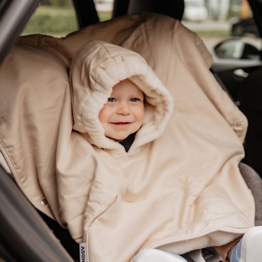 A toddler is sitting in a car seat and wearing a poncho with a hood