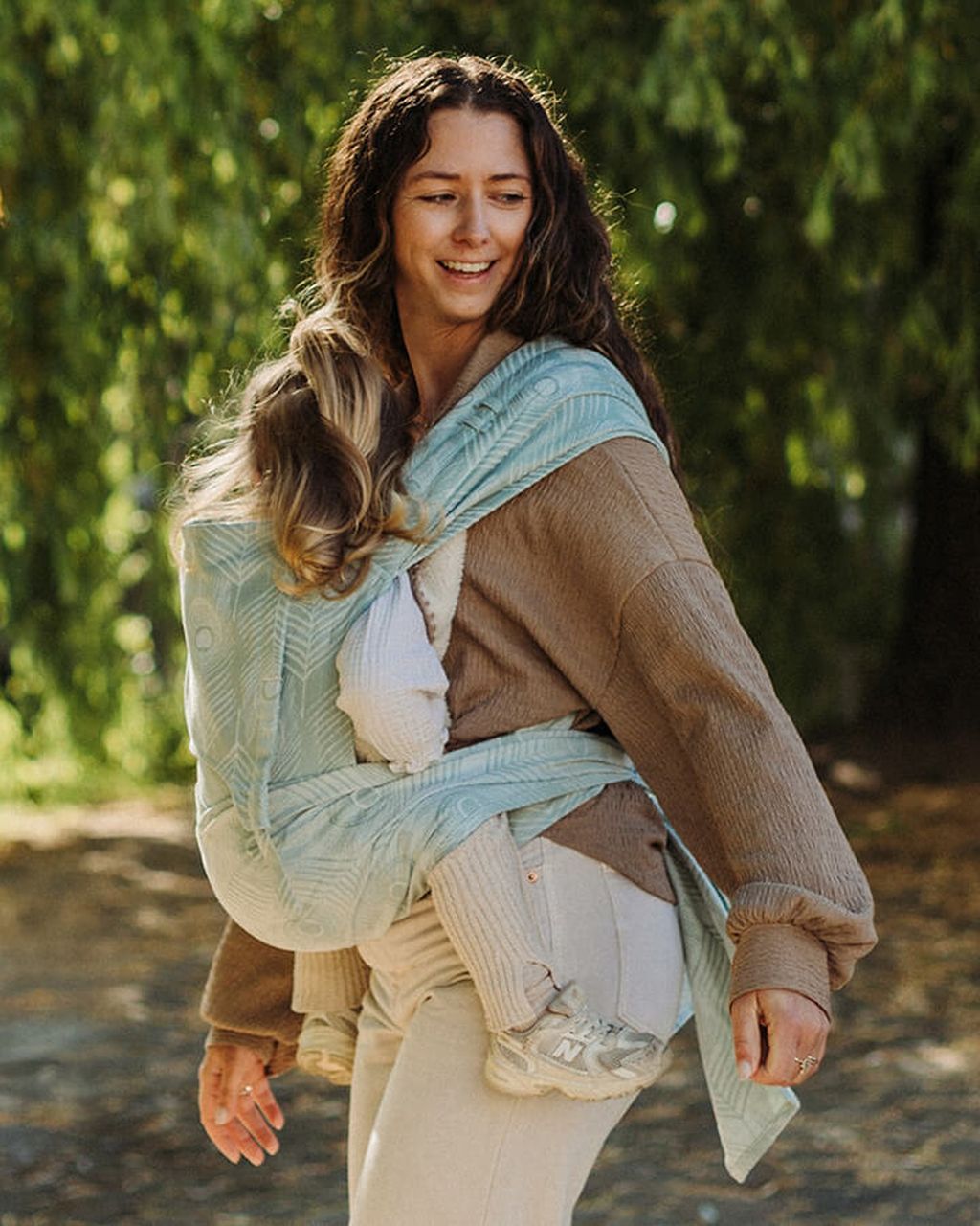 A woman smiles while carrying a baby in a Fly Click baby carrier
