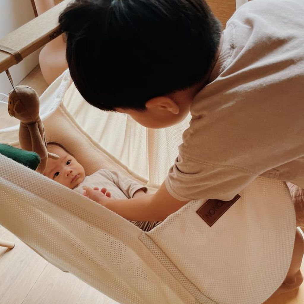 Ein kleines Kind schaut sanft auf ein Baby, das in einer gemütlichen Federwiege liegt