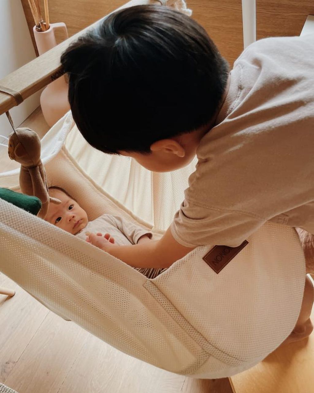 Ein kleines Kind schaut sanft auf ein Baby, das in einer gemütlichen Federwiege liegt