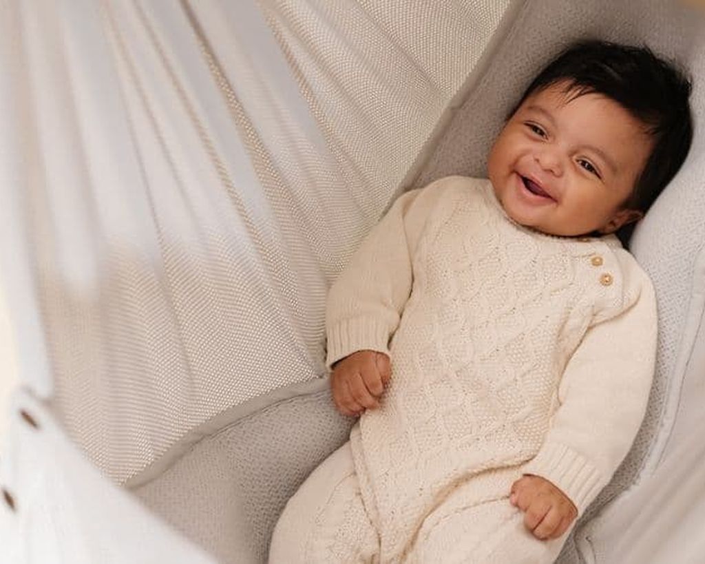 A happy baby smiling while lying in a cozy hammock