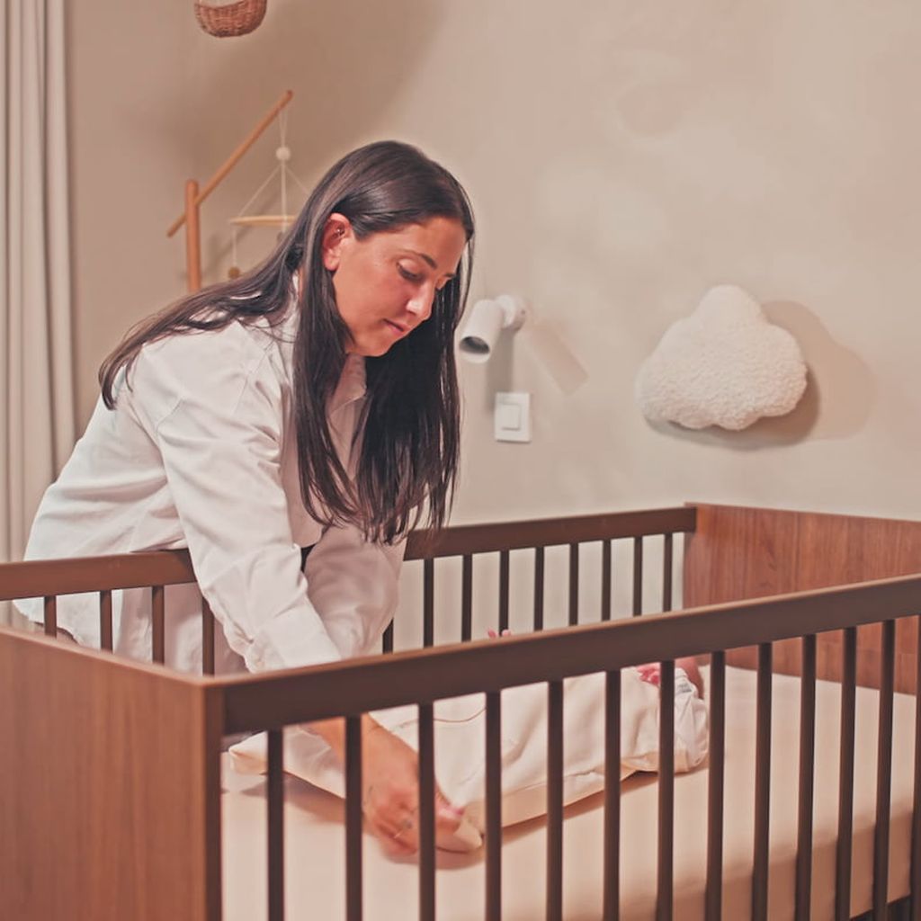 Een moeder doet haar kind, dat op bed ligt, de Bag Newborn slaapzak aan