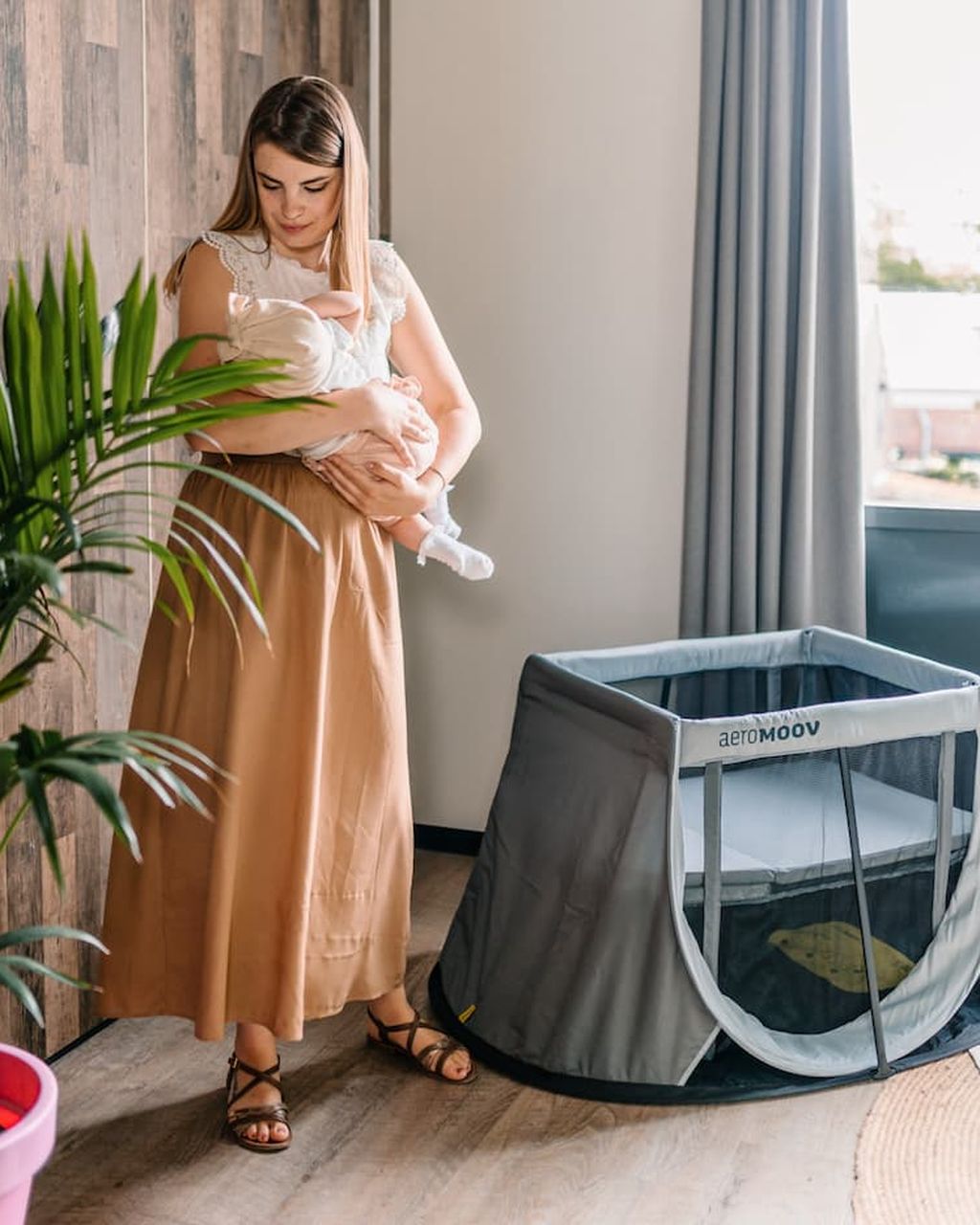 Eine Mutter hält ihr Baby neben einem AeroMoov-Reisebett.