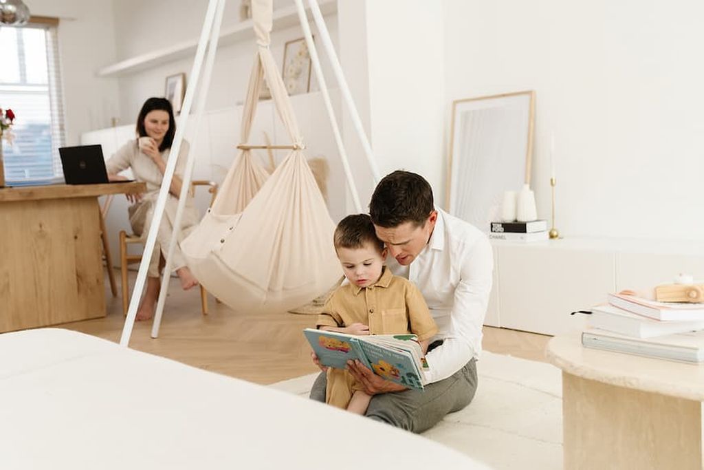 Ein Vater liest seinem Kleinkind ein Buch vor. Im Hintergrund hängt das NONOMO im Tipi-Ständer.