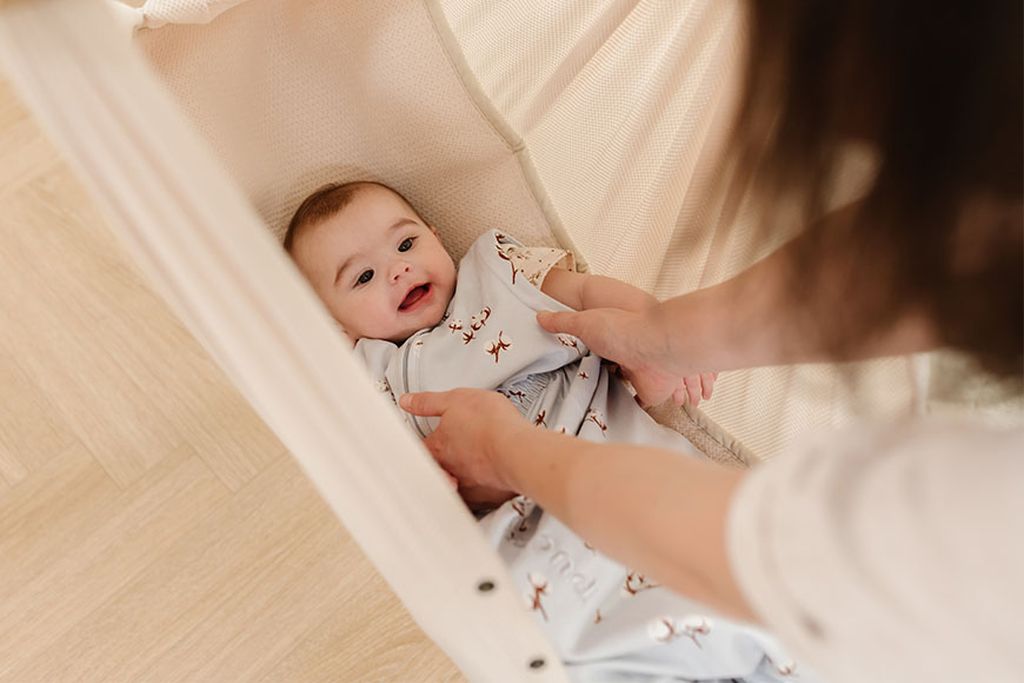 Das lächelnde Baby wird in die NONOMO-Hängematte gelegt.