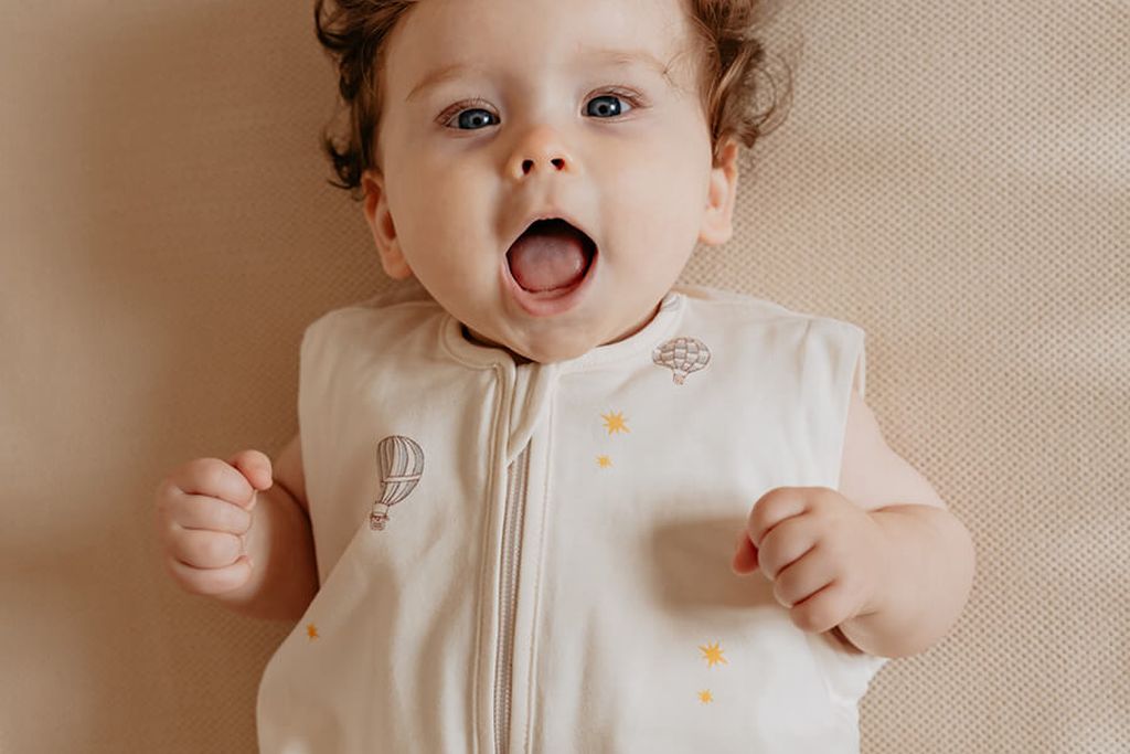 Baby met krullend haar, gekleed in een Puckababy Bag Newborn slaapzak met Balloons-print.