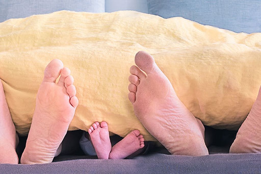 Familie im Bett. Über einer Decke sind nur ihre Füße zu sehen.