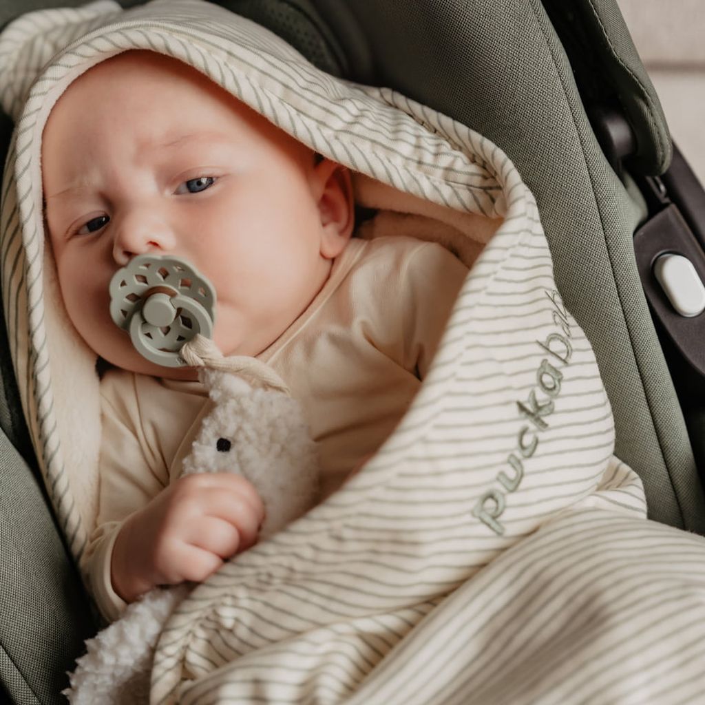 Een baby ligt rustig in een kinderwagen, gewikkeld in een Puckababy Gogo-wikkeldeken met Green Stripes-print.