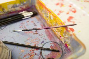 Een plastic bak met allerlei gekleurde verfvegen, met daarin een aantal kleine kwasten.