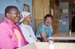 Drie deelnemers schieten in de lach terwijl ze op een bankje zitten in De Kadoeler.