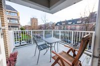 Ruim vierkant balkon met uitzicht op de buurt, met 2 tafeltjes en 3 stoelen en paarse heide in een plantenbak