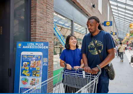Samen boodschappen doen bij de Lidl. De begeleider en deelnemer hebben samen een boodschappenwagen vast en zijn klaar om naar binnen te gaan.