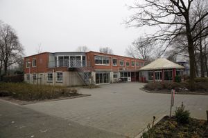 Een gebouw met twee verdiepingen met een metalen trap naar de tweede verdieping. Rechts aan het gebouw zit een rond bijgebouw met wit puntdak.