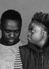 Een zwartwit portret van twee jonge mensen. De linker persoon kijkt naar beneden en de rechter kijkt naar de ander.