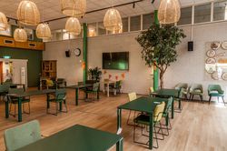 Gemeenschappelijke ruimte. Ingericht met groene tafels en stoelen.