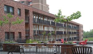 Aanzicht van appartementencomplex gezien vanaf een ruim dakterras met tafeltjes en stoelen