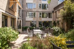 Zonnige binnentuin met een terras. Tuintafel met stoelen en veel planten om het terras.