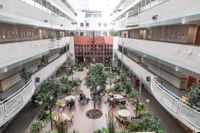 Gemeenschappelijke ruimte, waar de galerijen van de verdiepingen op uitkijken. Gezellig ingericht met tafels, stoelen, veel planten en veel lichtinval.