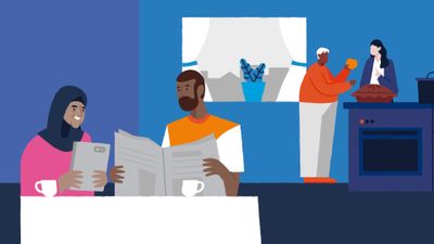 Een oudere dame met hoofddoek zit naast oudere heer met baard aan tafel, op de achtergrond een keuken met een heer met grijs haar en omvangrijke buik met jonge vrouw met lang zwart haar die een appaltaart uit de oven halen