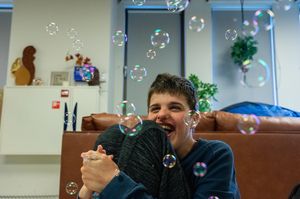 Een jongen zit in een woonkamer op de grond en kijkt omhoog naar allemaal geblazen bellen.