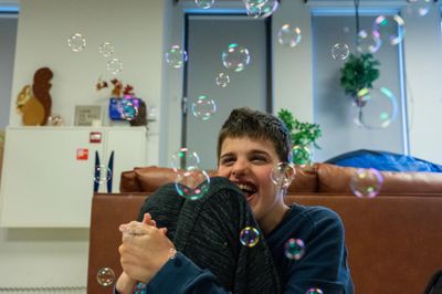 Een jongen zit in een woonkamer op de grond en kijkt omhoog naar allemaal geblazen bellen.