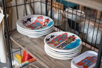 Een houten kast met borden, beschilderd met Amsterdamse grachtenpanden.