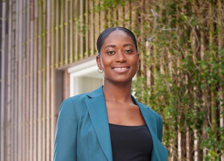 Een lachende vrouw met donker haar en een blauwe colbert aan.