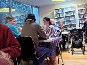 Een sfeervol verlichte ruimte met allemaal tafels met mensen eraan, die met elkaar in gesprek zijn.