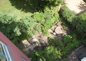 Een tuin van bovenaf gezien, met daarin veel groene planten en een ronde houten tafel met houten stoelen.